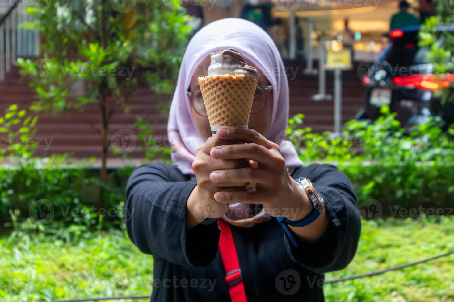ein asiatisch Muslim Frau halten ein Eis Sahne Kegel mit beide Hände. draußen. foto