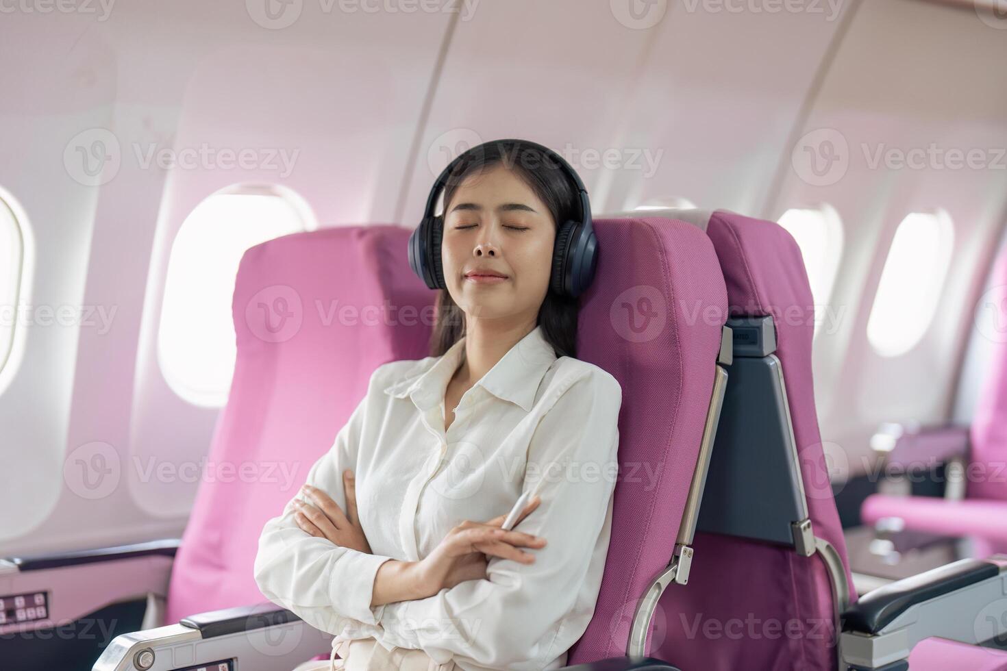 asiatisch Frau im Kabine tragen Kopfhörer ruhen während Hören zu Musik- im Flugzeug während Flug foto