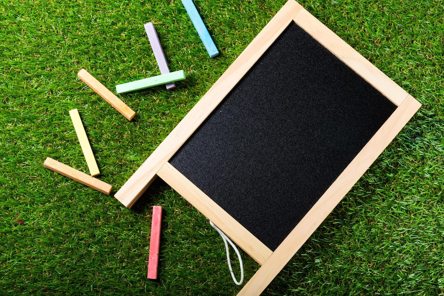 Draufsicht der Mini-Tafel und Farben auf Plastikgrashintergrund. Konzept zurück in die Schule foto