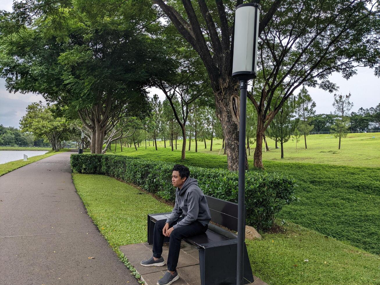 Mann sitzen auf das Grün Park Nieder Stadt. das Foto ist geeignet zu verwenden zum Ruhe genossen Aktivität, Freizeit Aktivität und Park Hintergrund.