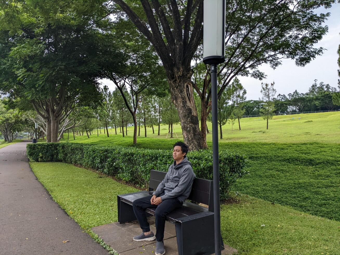 Mann sitzen auf das Grün Park Nieder Stadt. das Foto ist geeignet zu verwenden zum Ruhe genossen Aktivität, Freizeit Aktivität und Park Hintergrund.