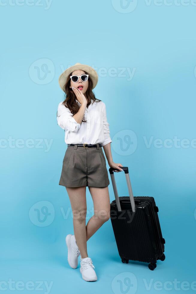 schockiert und überrascht schön asiatisch weiblich Tourist Tragen Gepäck gehen auf ein Ausflug Stehen isoliert auf Blau Hintergrund. Kopieren Raum foto
