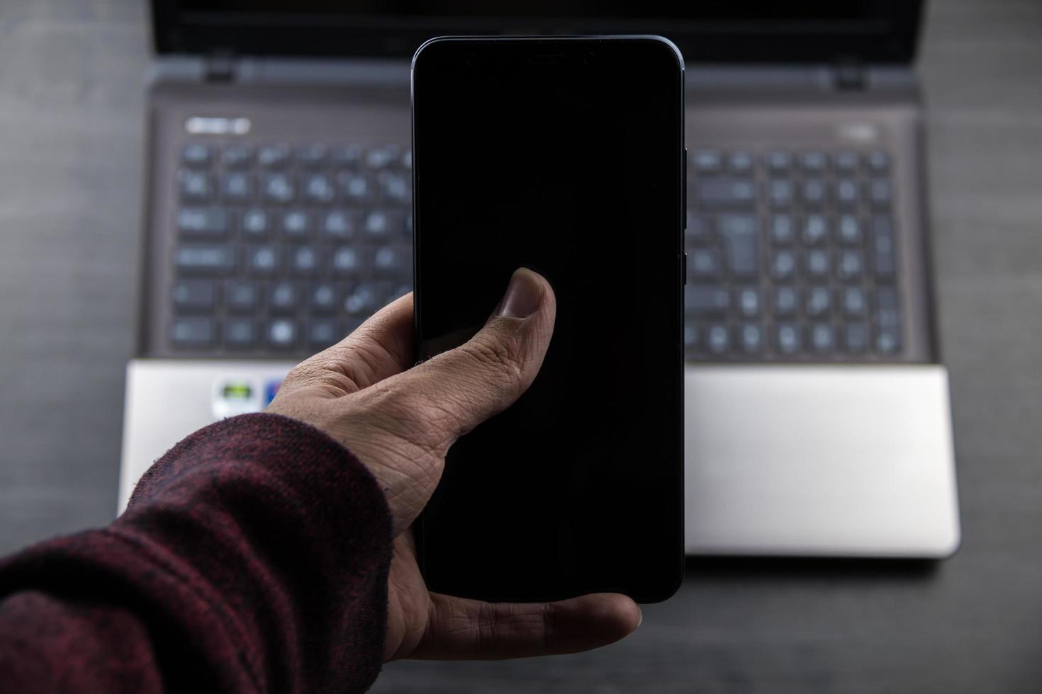 Hand mit einem modernen Handy und einem Laptop-Hintergrund foto