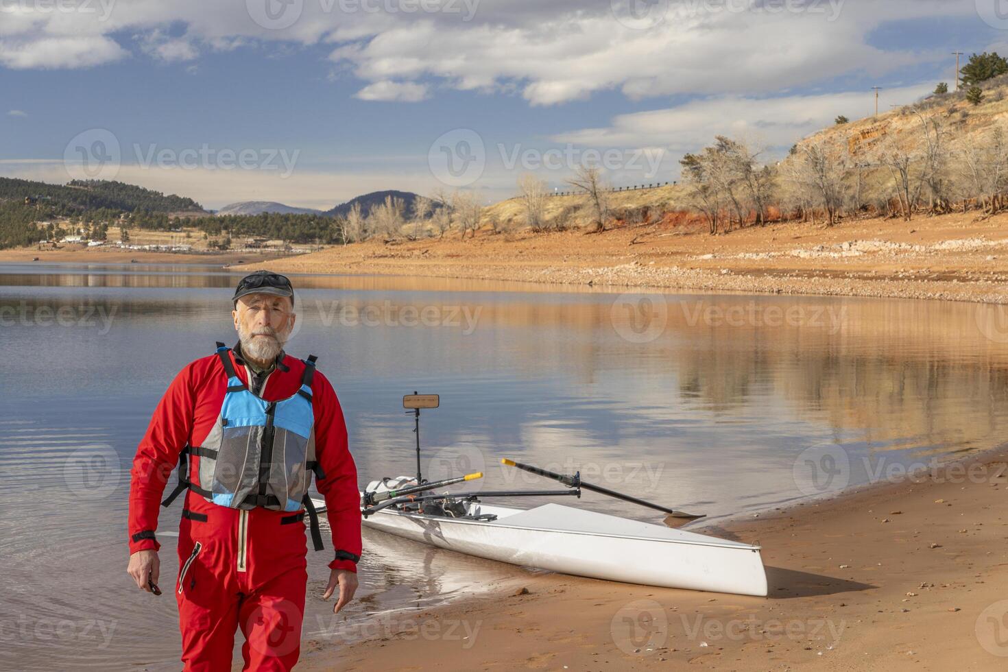Senior Mann tragen Trockenanzug und Leben Jacke mit ein Rudern Schale auf See Ufer foto
