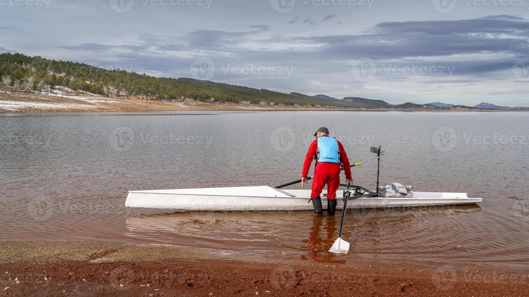 Senior männlich Ruderer ist Starten ein Rudern Schale auf ein Ufer von Fuhrmann See im Nord Colorado im Winter Landschaft. foto