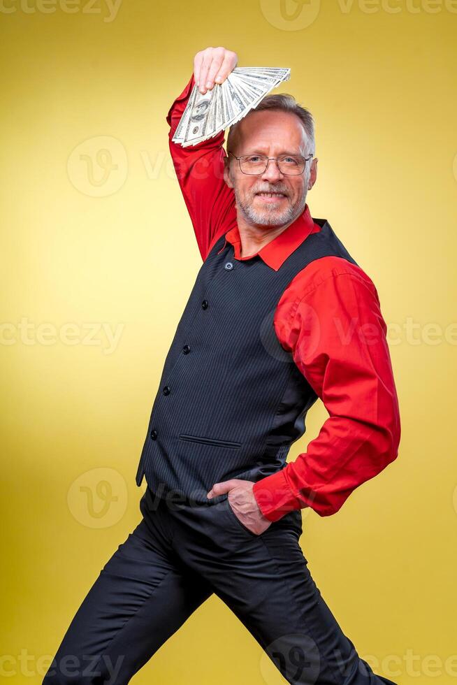 alt lächelnd grauhaarig Mann im Brille halten Ventilator von Dollar Über Kopf im Tanzen Pose. Mensch Emotionen und Gesichts- Ausdrücke foto