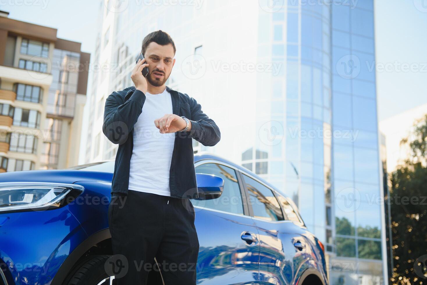 Porträt von ein jung Mann mit ein Handy, Mobiltelefon Telefon im seine Hand in der Nähe von ein Auto auf ein Sommer- Straße. foto