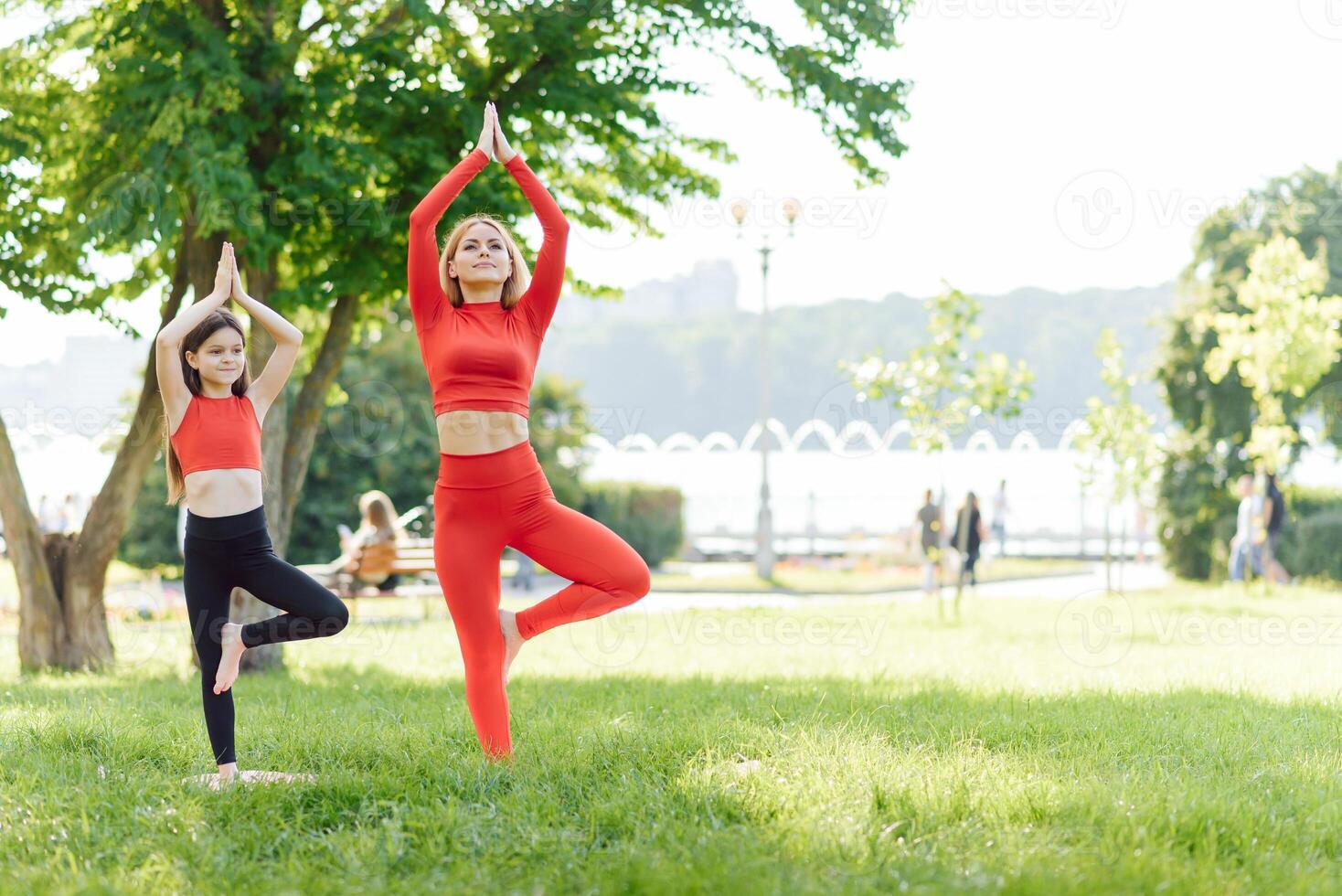 ein jung Mutter und Tochter im Sportbekleidung tun Yoga zusammen im ein Park. das Konzept von ein Familie Urlaub. Sport, Fitness, Meditation foto