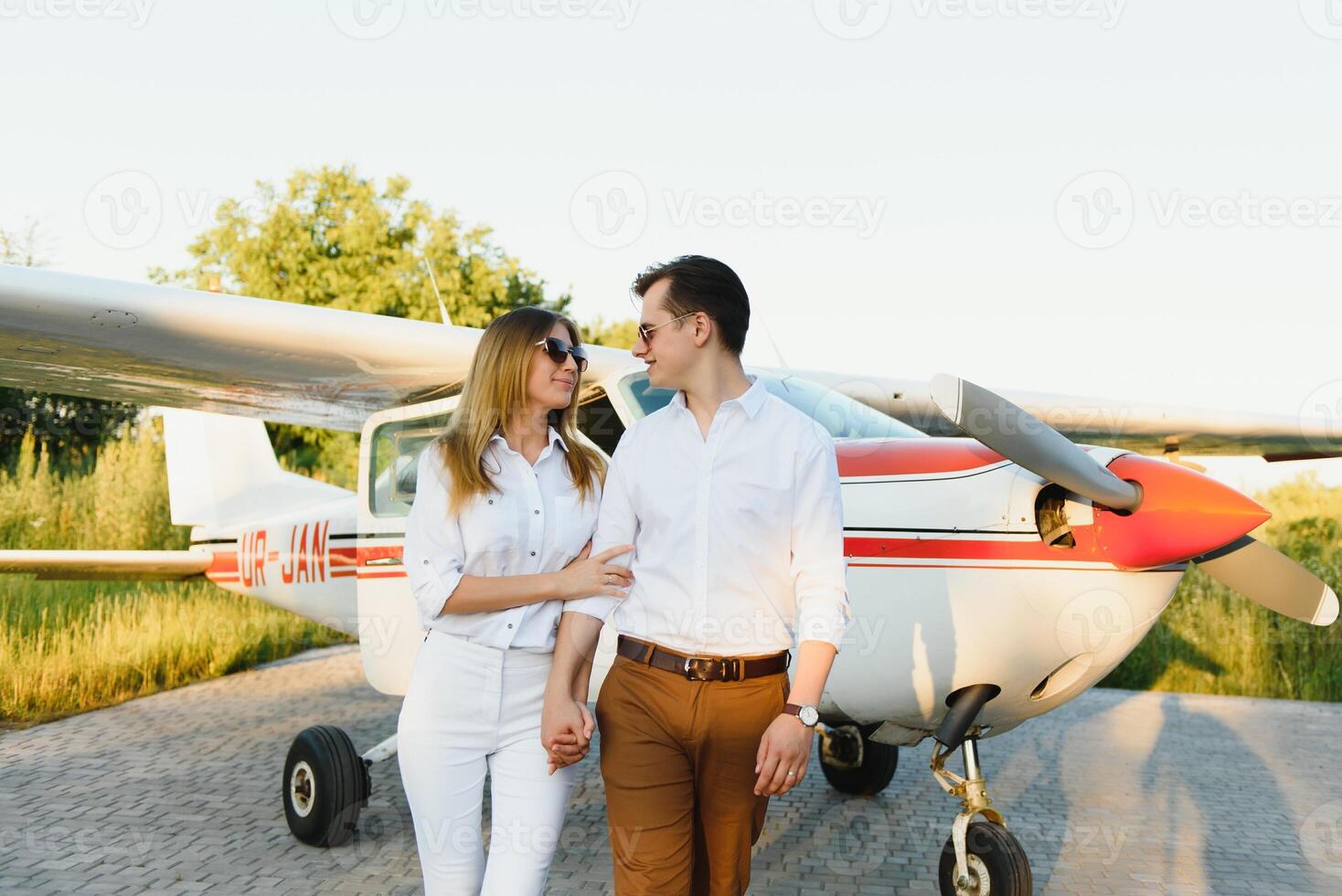 in voller Länge Bild von schön jung stilvoll Paar in der Nähe von Privat Ebene. Gehen auf Runway im Flughafen im Vorderseite von Flugzeug. foto