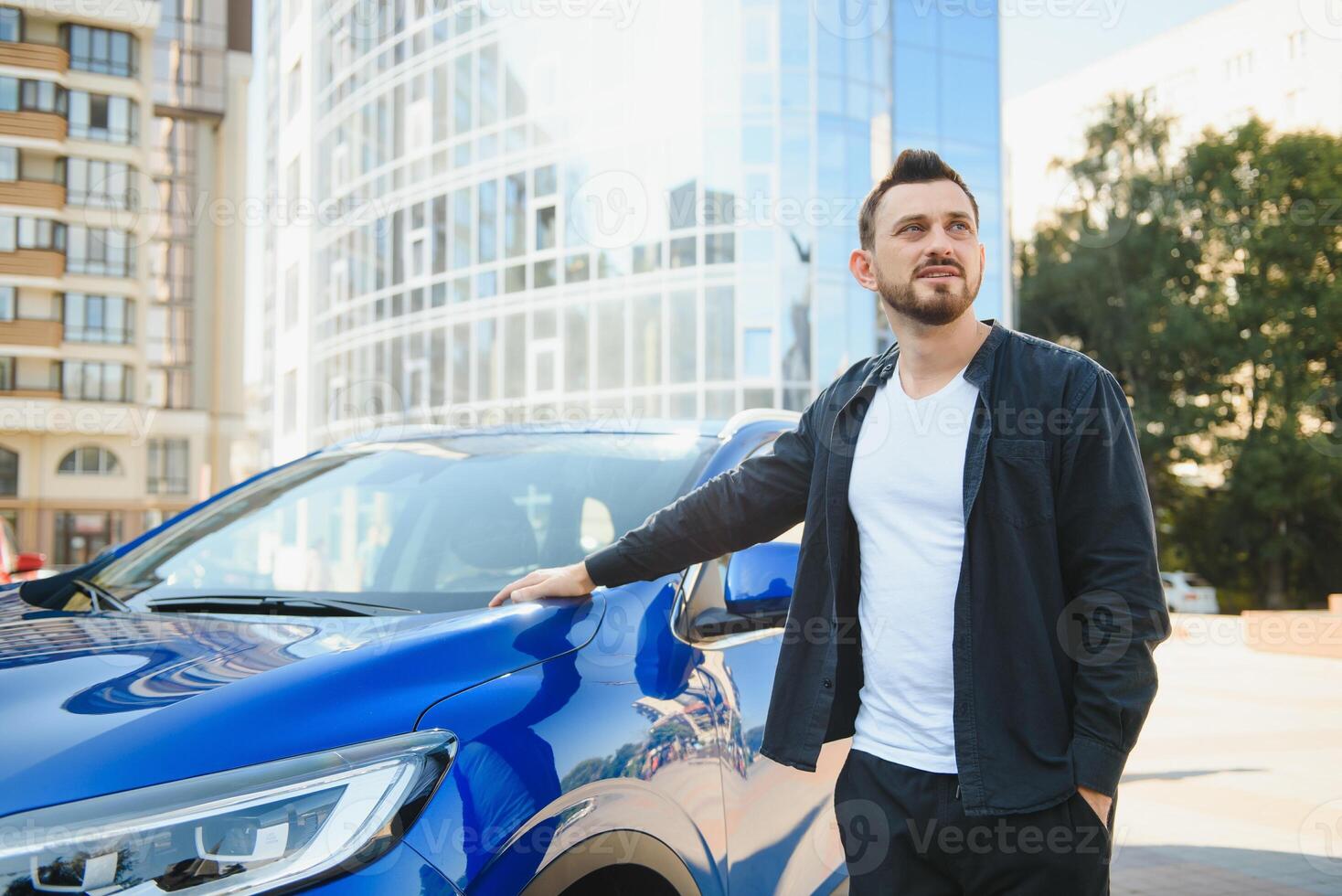 Porträt von ein jung Mann mit ein Handy, Mobiltelefon Telefon im seine Hand in der Nähe von ein Auto auf ein Sommer- Straße. foto