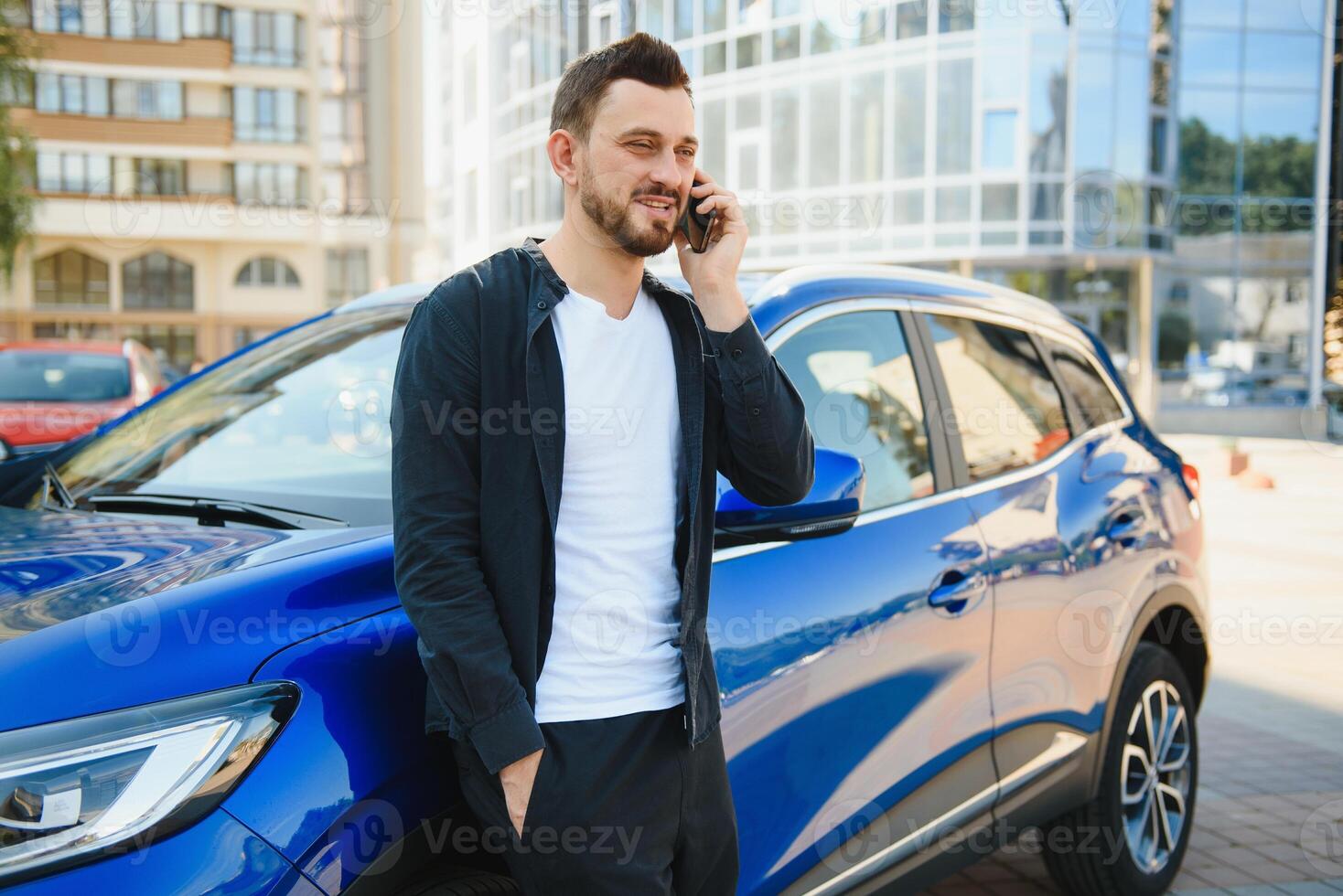 Porträt von ein jung Mann mit ein Handy, Mobiltelefon Telefon im seine Hand in der Nähe von ein Auto auf ein Sommer- Straße. foto