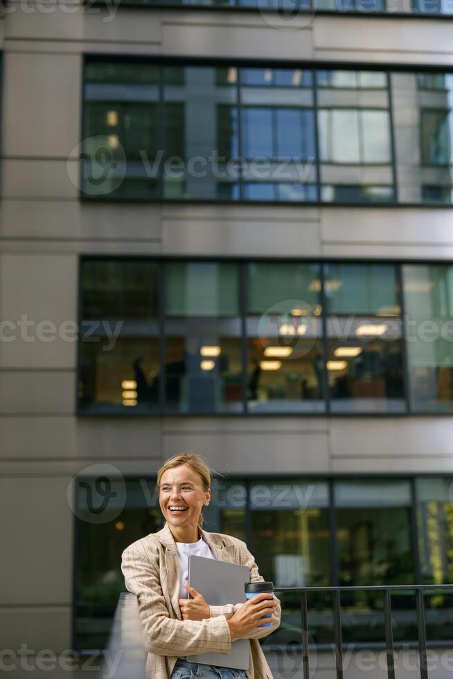 Geschäft Frau Stehen mit Laptop und Kaffee auf Büro Terrasse während brechen Zeit und sieht aus Weg foto