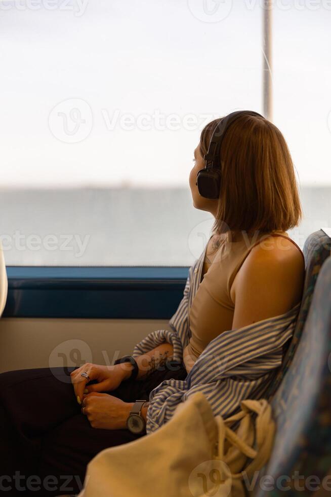 Frau im Kopfhörer während Reisen im Öffentlichkeit Transport und suchen Aussicht draußen das Fenster foto