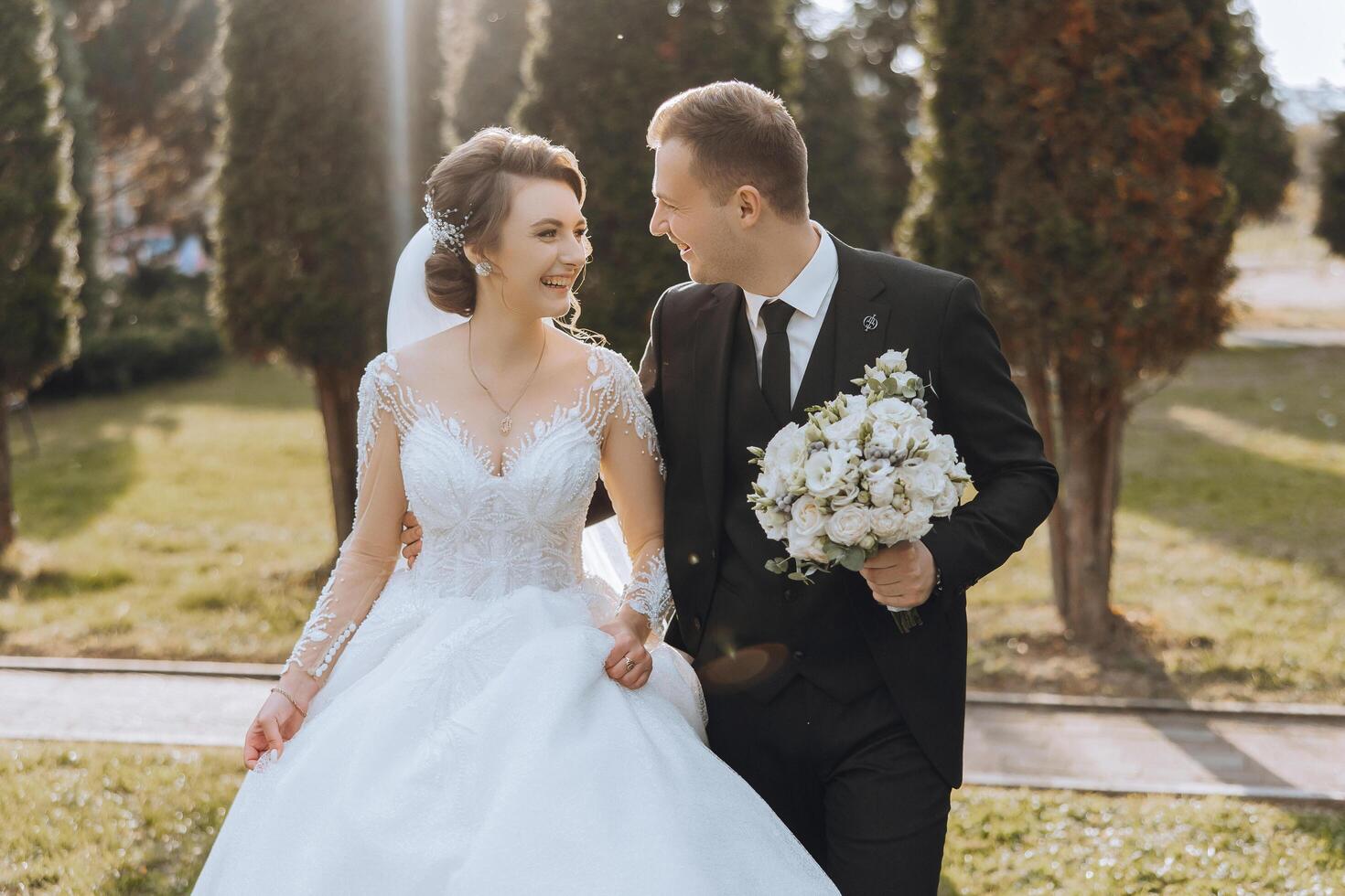 ein Hochzeit Paar ist Gehen im Natur auf ein Herbst Tag. glücklich jung Braut und elegant Bräutigam halten Hände. ein stilvoll Paar von Jungvermählten auf ihr Hochzeit Tag. foto