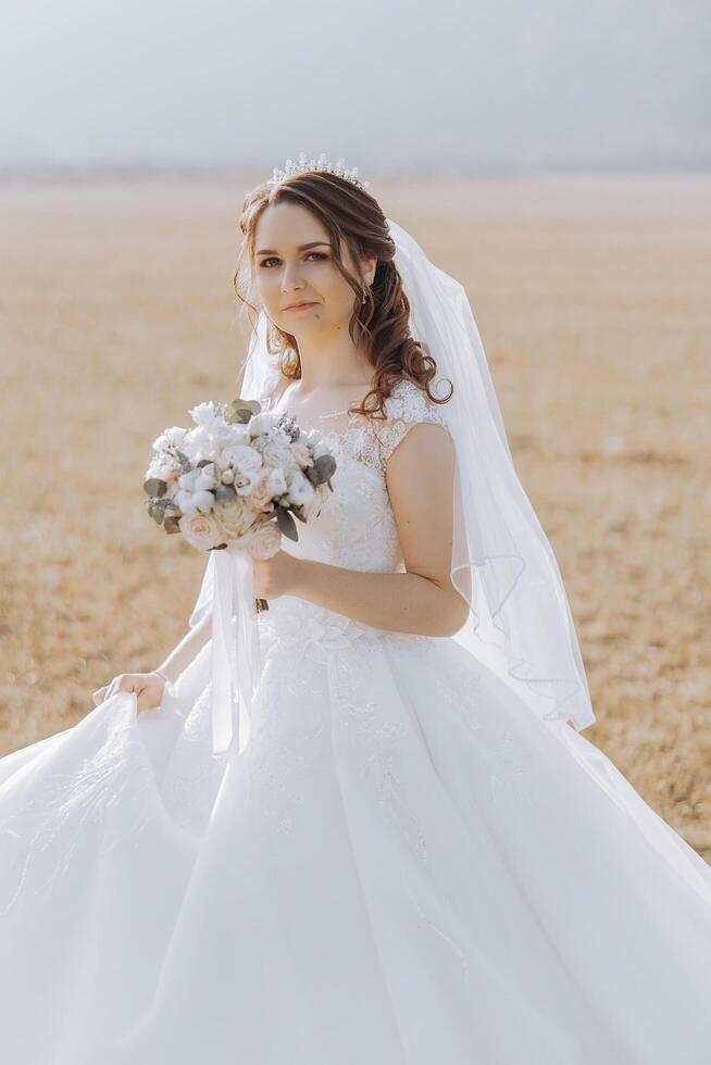 Porträt. ein Brünette Braut im ein Kleid und ein Schleier, mit ein schick Krone, posiert mit ein Strauß. Silber Schmuck. schön bilden und Haar. Herbst Hochzeit. Feier foto