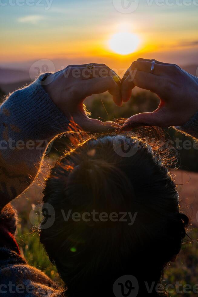 Ein junges Mädchen, das bei Sonnenuntergang mit ihren Händen ein Herzsymbol macht foto