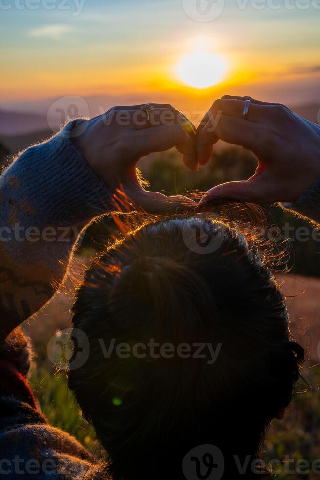 Ein junges Mädchen, das bei Sonnenuntergang mit ihren Händen ein Herzsymbol macht foto