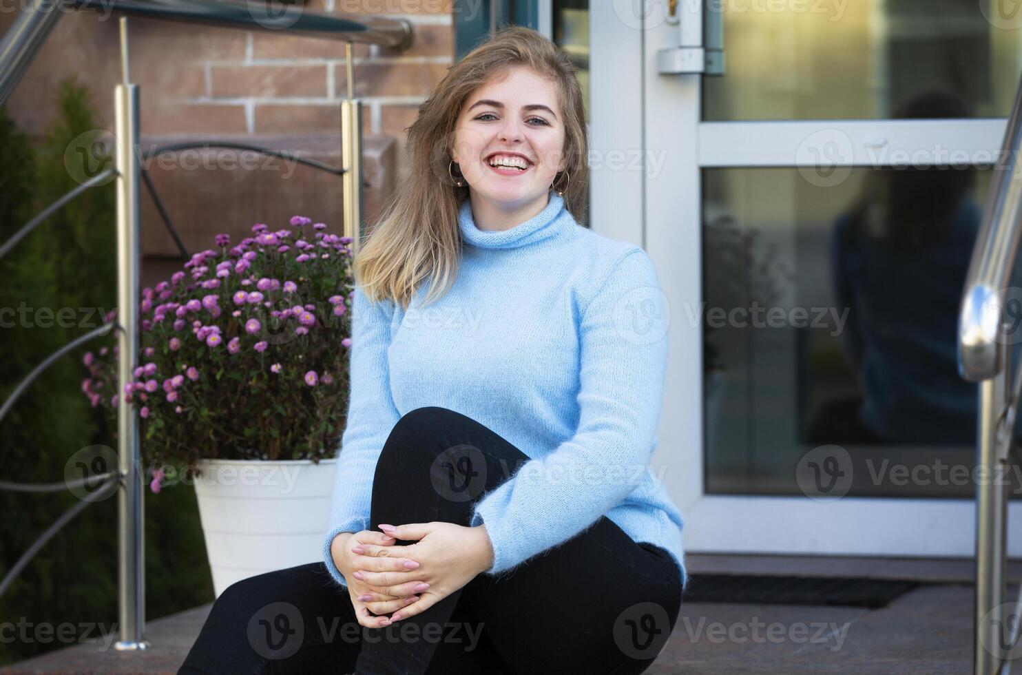 auf das Straße, ein glücklich blond Mädchen im ein Blau gestrickt Pullover. foto