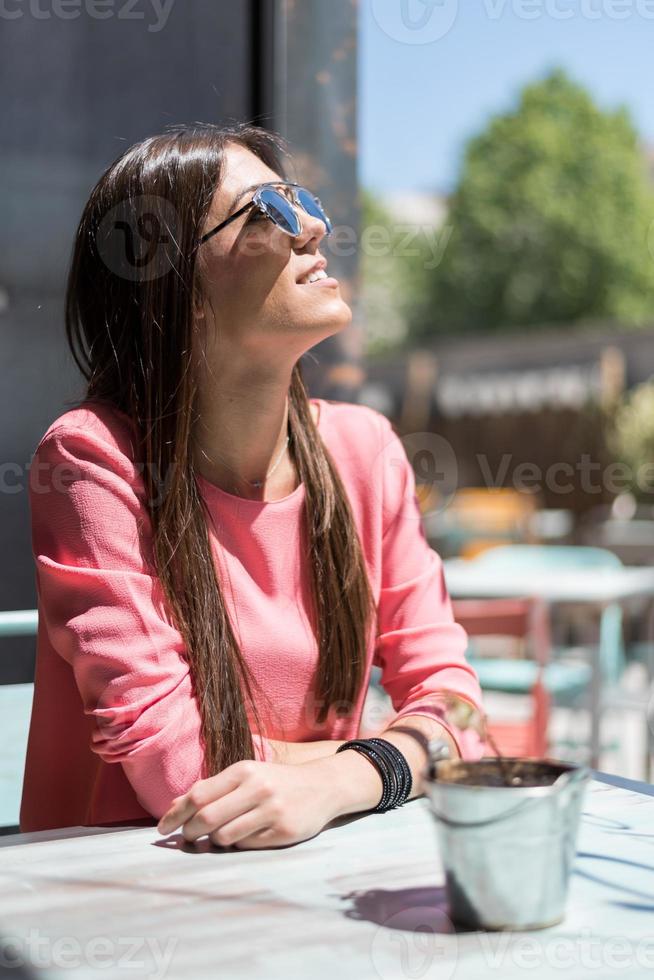 glückliche junge Frau sitzt auf einer Restaurantterrasse mit Sonnenbrille foto