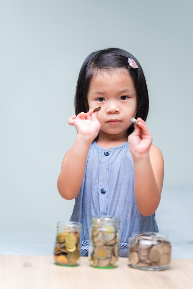 Porträt abgebildet. asiatisches Kindermädchen, das Silbermünzen in ihren Händen hält. Geld für die Zukunft sparen. Münzen Bargeld im Graskrug. auf Holztisch. isolierter sauberer Hintergrund. foto
