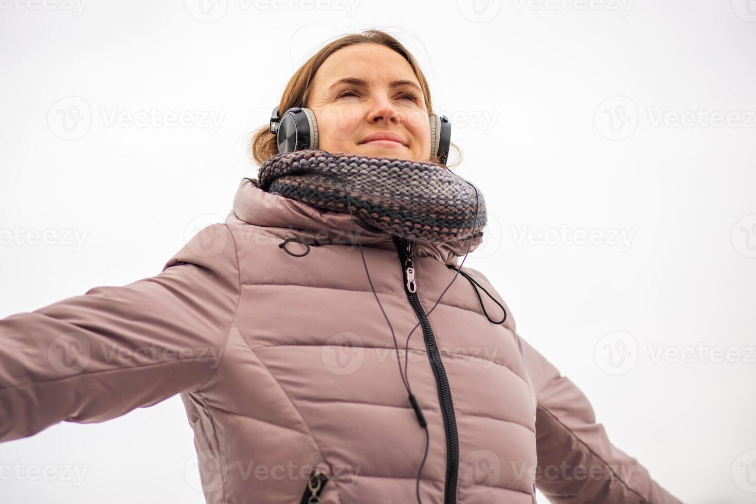 froh jung Frau im Jacke Hören zu Musik, entspannend im ein Park foto