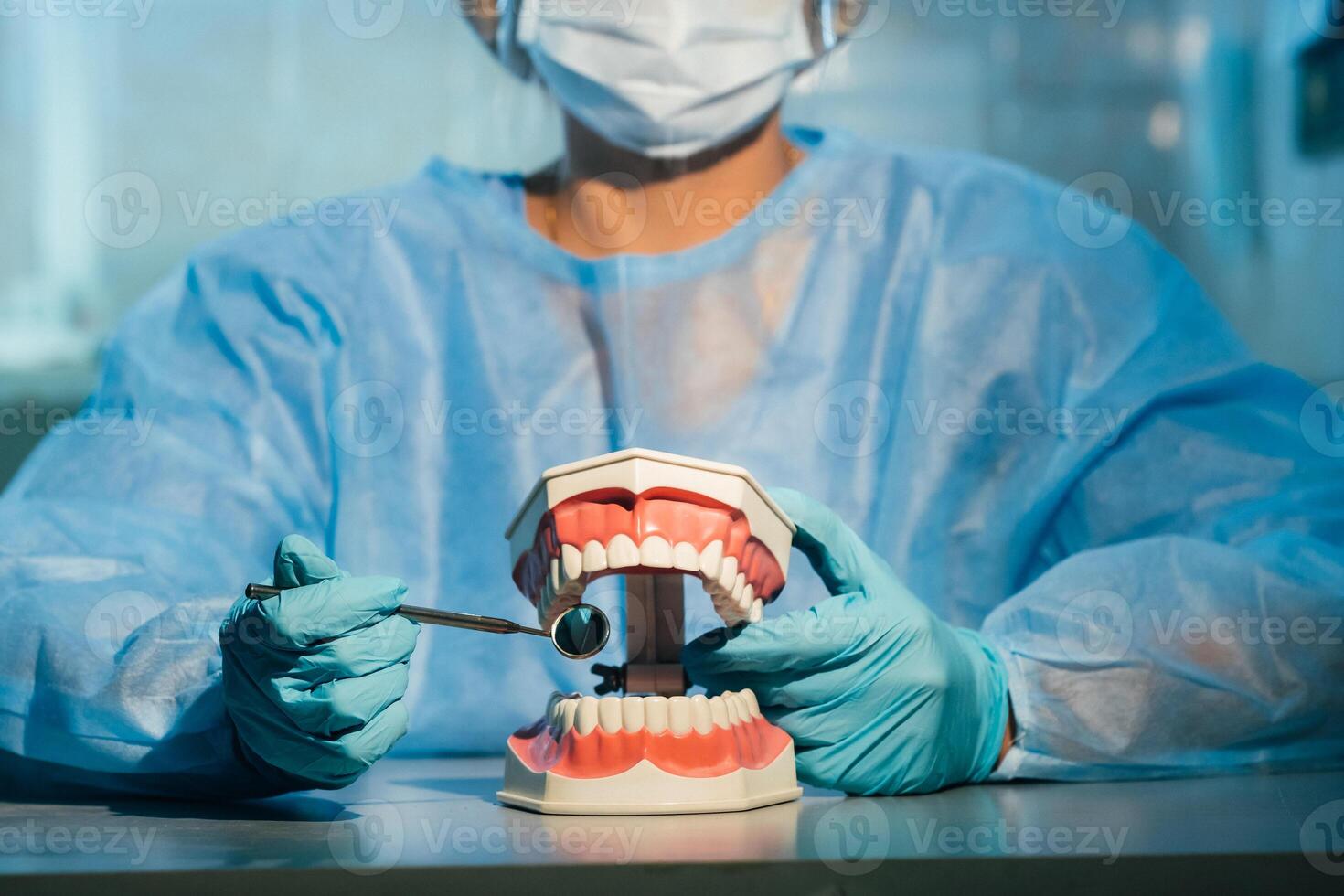 ein Dental Arzt tragen Blau Handschuhe und ein Maske hält ein Dental Modell- von das Oberer, höher und niedriger Kiefer und ein Dental Spiegel foto