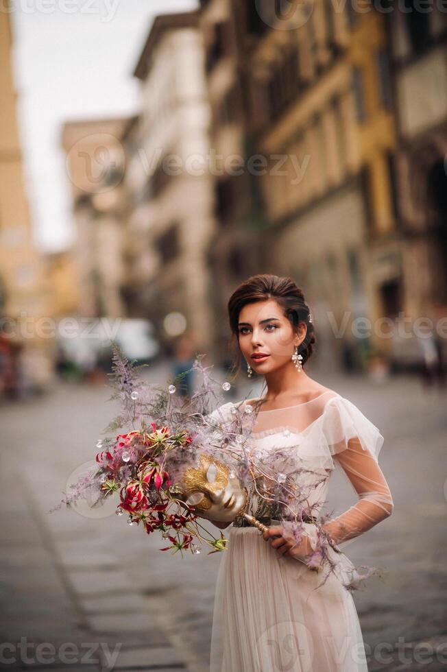 das Mädchen-Braut ist mit schön Blume Muster wie ein Maske im Florenz, stilvoll Braut im ein Hochzeit Kleid Stehen mit ein Maske im das alt Stadt, Dorf von Florenz. Modell- Mädchen im Florenz foto