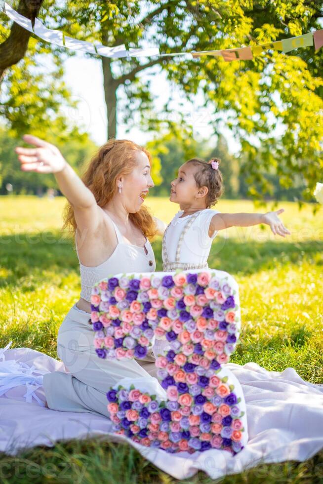 heiter Mutter und Tochter haben Spaß auf Kind Geburtstag auf Decke mit Papier Dekorationen im das Park foto