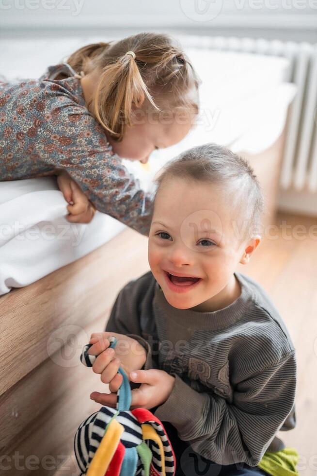 klein Junge mit Nieder Syndrom Theaterstücke mit seine jünger Schwester auf das Bett im Zuhause Schlafzimmer. hoch Qualität Foto