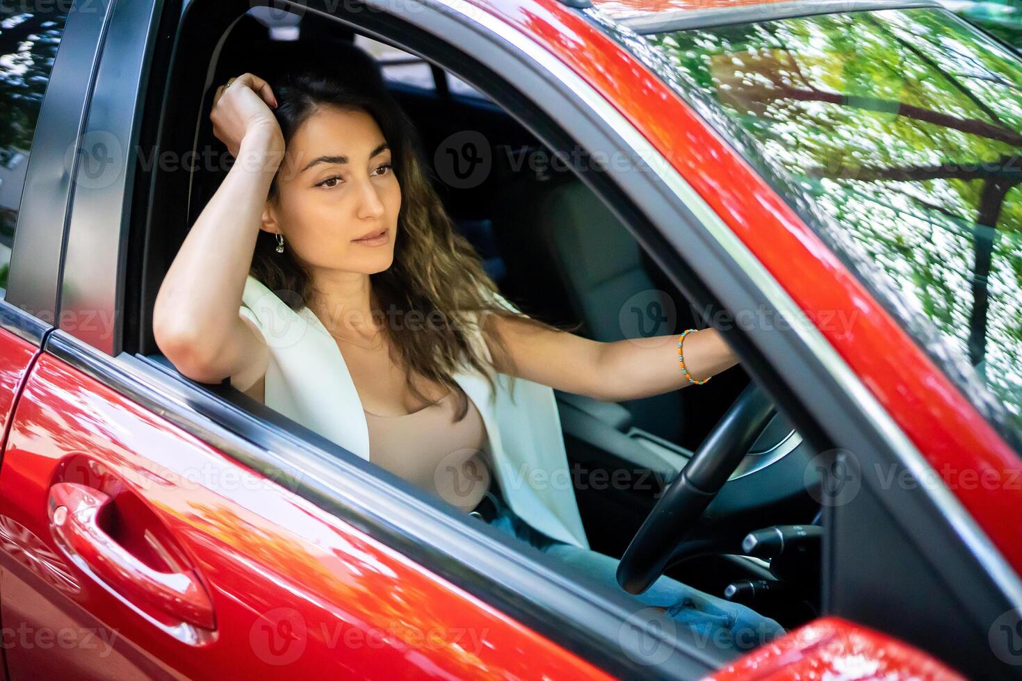 glücklich lächelnd Frau Treiber hinter das Rad rot Wagen. Aussicht durch Auto Fenster foto