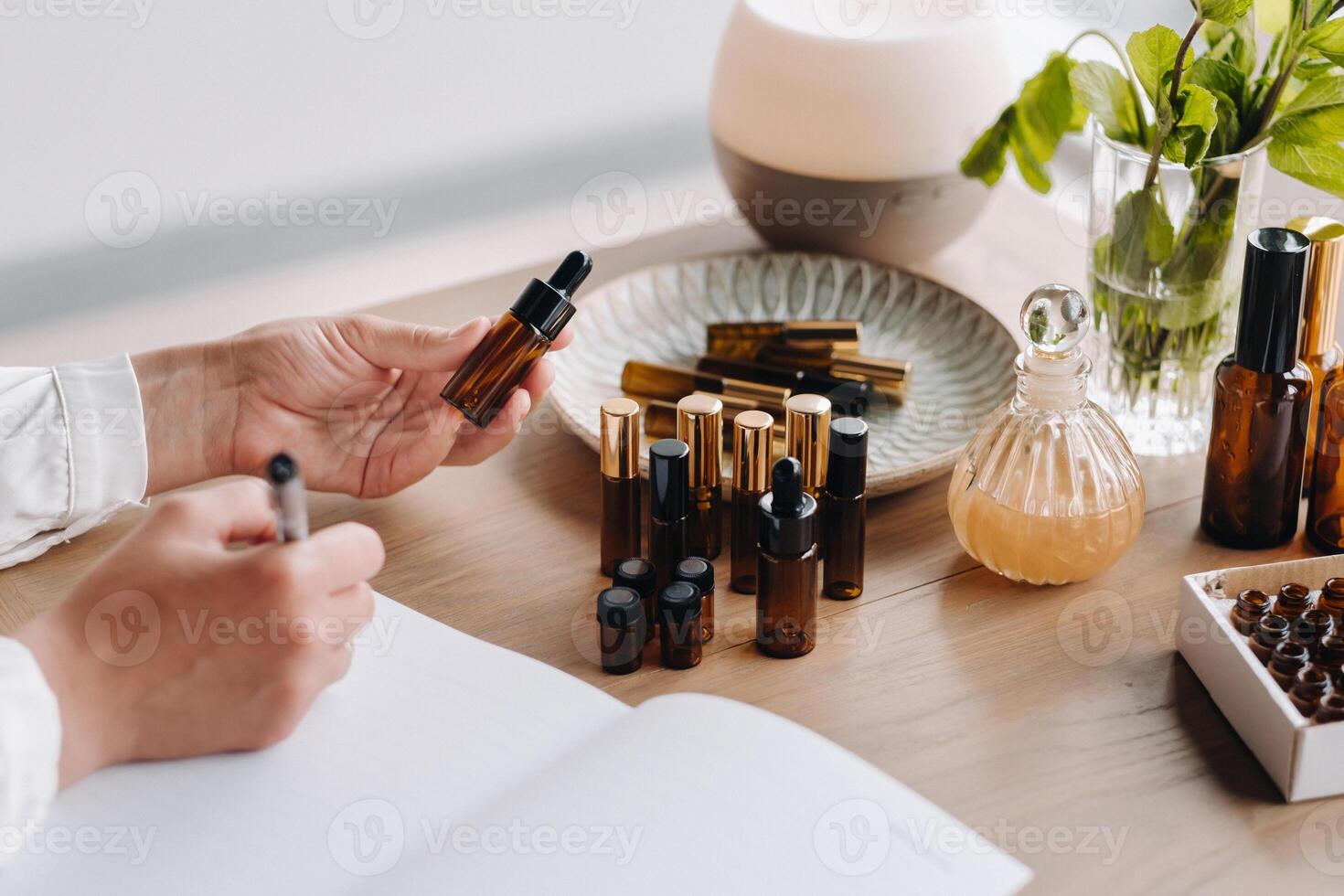 Nahansicht von weiblich Hände halten ein Flasche von wesentlich Öl und Schreiben ein Eintrag im ein Notizbuch, Aromatherapie foto