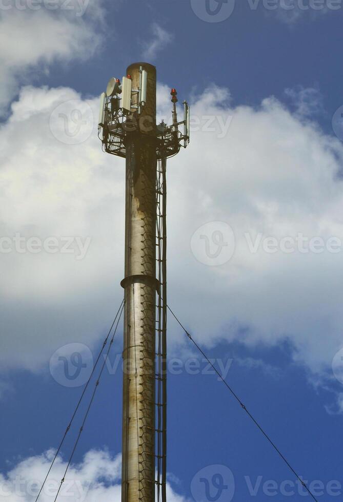 Hoher Metallschornstein einer Industrieanlage mit Leiter in Form von Metallstreben vor dem Hintergrund eines bewölkten blauen Himmels foto