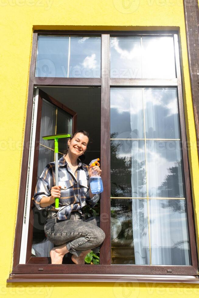 ein Frau manuell wäscht das Fenster von das Haus mit ein Lappen mit ein sprühen Reiniger und ein Mopp außen. Sicherheit beim Höhe, Wiederherstellen bestellen und Sauberkeit im das Frühling, Reinigung Bedienung foto