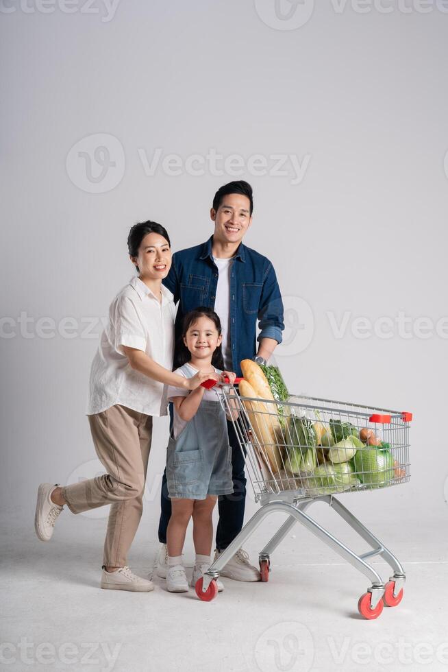 Bild von asiatisch Familie schieben ein Supermarkt Wagen während Einkaufen, isoliert auf Weiß Hintergrund foto