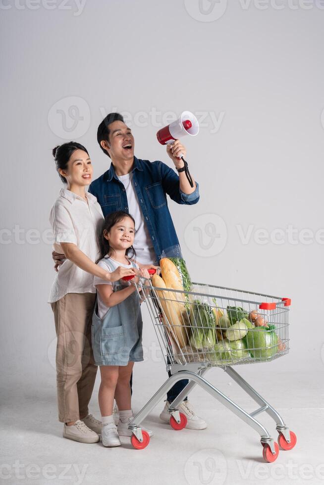 Bild von asiatisch Familie schieben ein Supermarkt Wagen während Einkaufen, isoliert auf Weiß Hintergrund foto