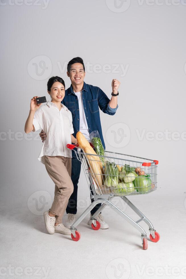 Bild von asiatisch Paar schieben Supermarkt Wagen während Einkaufen, isoliert auf Weiß Hintergrund foto