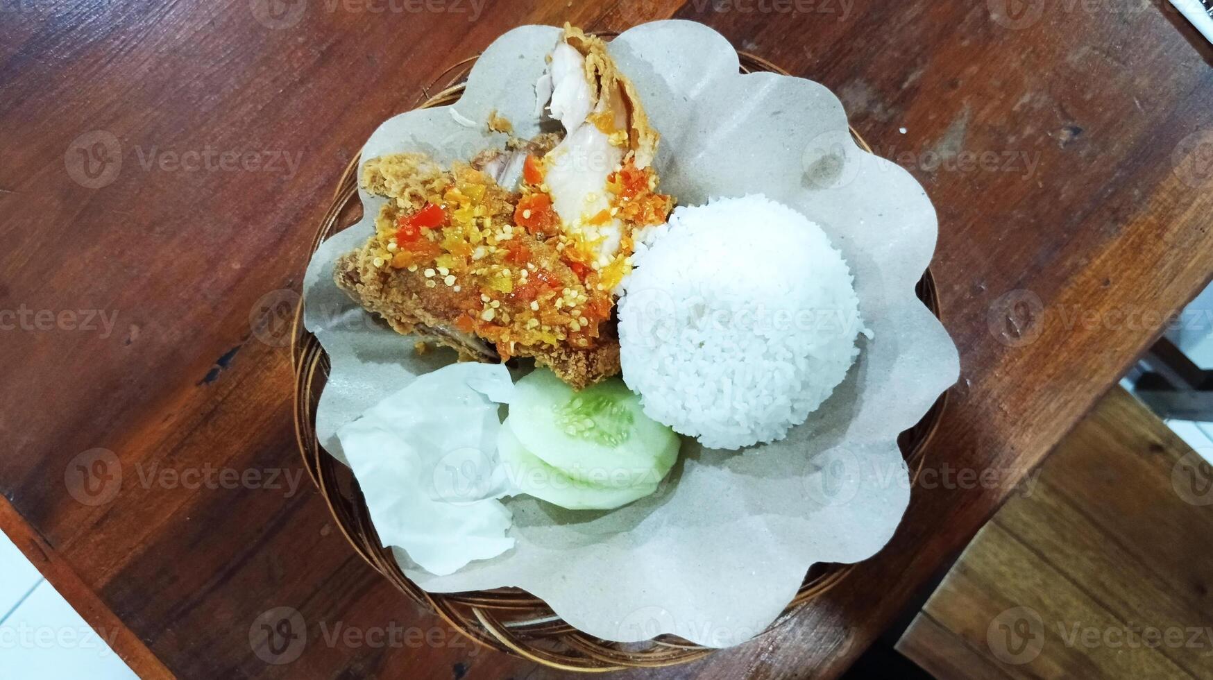 Ayam geprek indonesisch Essen knusprig gebraten Hähnchen mit würzig Chili Soße serviert mit Reis und frisch Gemüse foto