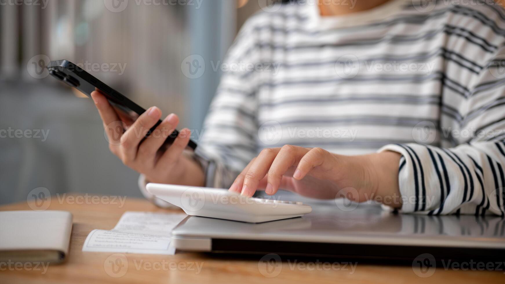 ein abgeschnitten Schuss von ein Frau mit ihr Smartphone und ein Taschenrechner beim ein Schreibtisch, rechnen ihr Rechnungen. foto