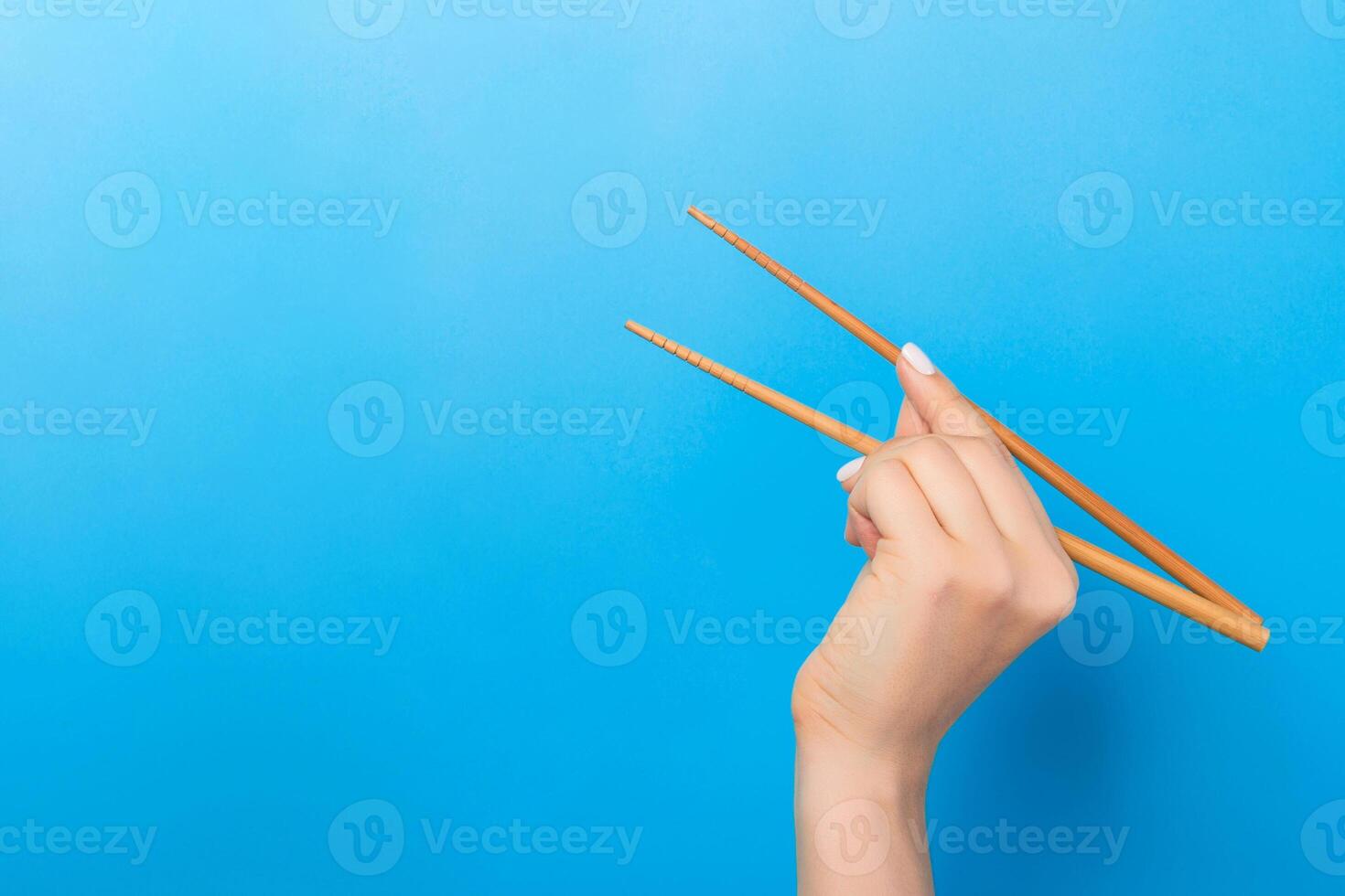 Die Hand des Mädchens zeigt Essstäbchen auf blauem Hintergrund. asiatisches küchenkonzept mit leerem raum für ihr design foto