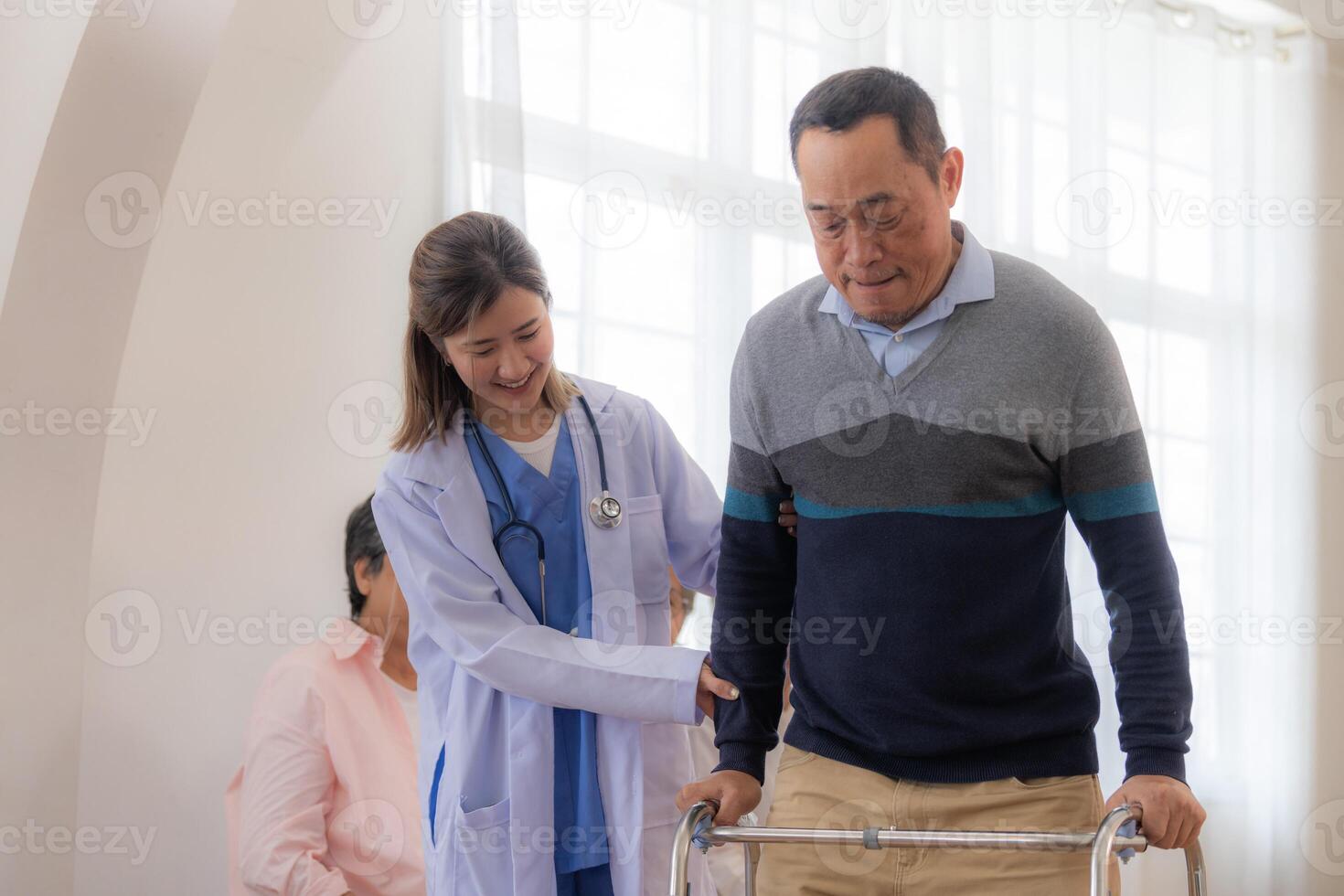 asiatisch jung Krankenschwester Unterstützung Senior älter Mann gehen mit Gehhilfe. schön Krankenschwester Hilfe und nehmen Pflege. Alten reifen Opa geduldig tun physisch Therapie mit ein Gruppe von Senior freunde im Krankenhaus. foto