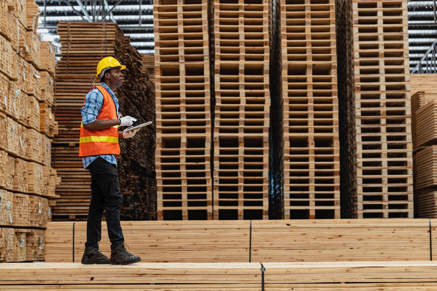 afrikanisch Arbeitskräfte Mann Ingenieurwesen Gehen und inspizieren mit Arbeiten Suite Kleid und Hand Handschuh im Bauholz Holz Lagerhaus. Konzept von Clever Industrie Arbeiter Betriebs. Holz Fabriken produzieren Holz Gaumen. foto