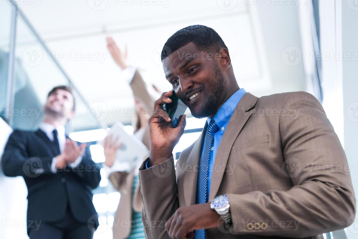 Clever schwarz Geschäftsmann Aufpassen Handy, Mobiltelefon Telefon. kahl Erwachsene Mann tragen formal tragen. nachdenklich Afroamerikaner Geschäftsmann im ein perfekt maßgeschneidert passen Stehen im Treppe im Büro. foto