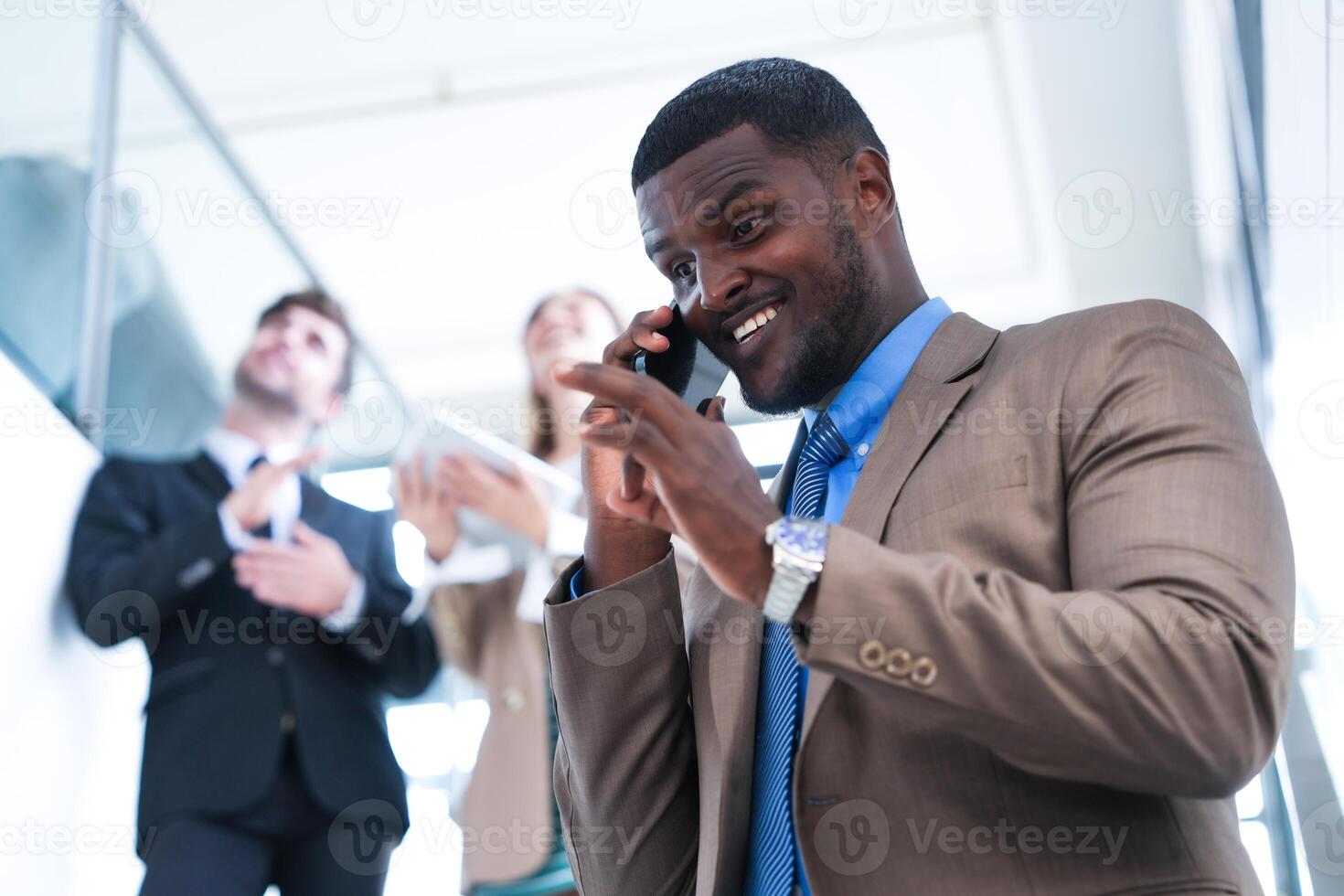 Clever schwarz Geschäftsmann Aufpassen Handy, Mobiltelefon Telefon. kahl Erwachsene Mann tragen formal tragen. nachdenklich Afroamerikaner Geschäftsmann im ein perfekt maßgeschneidert passen Stehen im Treppe im Büro. foto