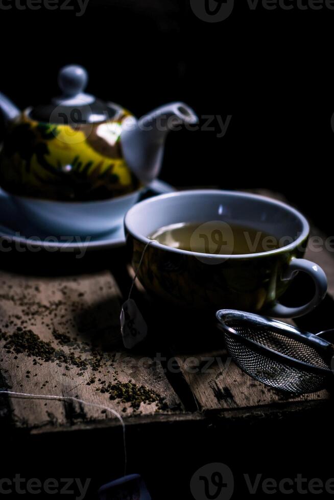 Tee Tasse und Teekanne auf das hölzern Tabelle mit schwarz Hintergrund foto