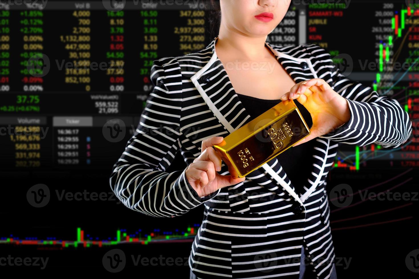 Geschäftsfrau, die den Goldbarren am Handels- und Diagrammhintergrund hält foto