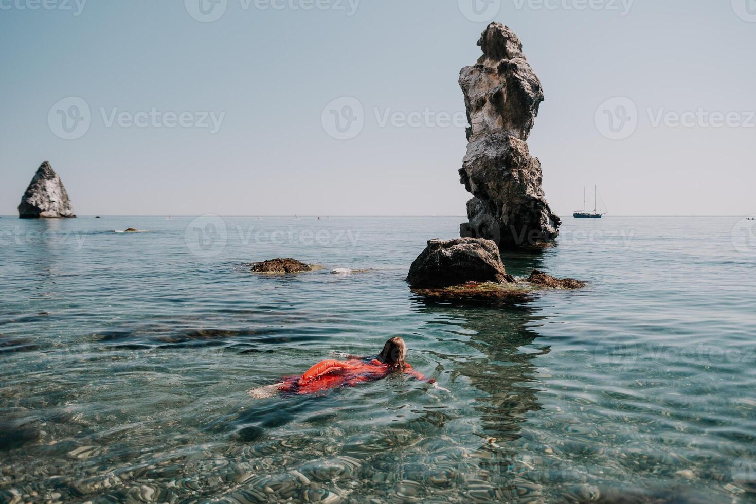 Frau Reise Meer. glücklich Tourist im rot Kleid genießen nehmen Bild draußen zum Erinnerungen. Frau Reisender posieren im Meer Strand, umgeben durch vulkanisch Berge, Teilen Reise Abenteuer Reise foto