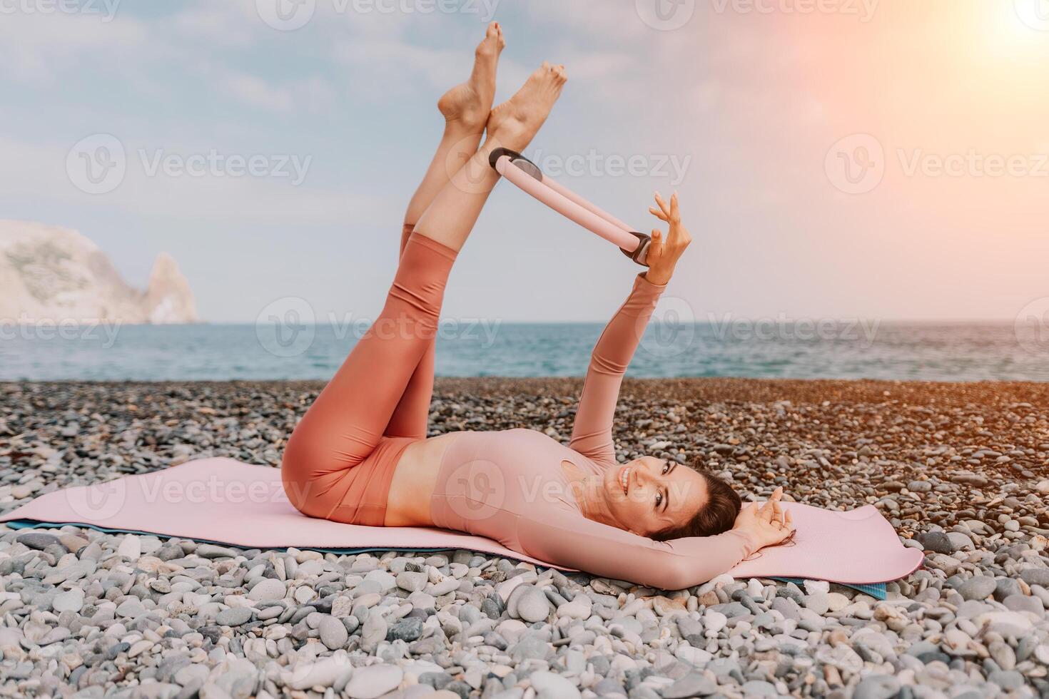 Frau Meer Pilates. sportlich glücklich Mitte alt Frau üben Fitness auf Strand in der Nähe von Meer, lächelnd aktiv weiblich Ausbildung mit Ring auf Yoga Matte außen, genießen gesund Lebensstil, Harmonie und Meditation foto