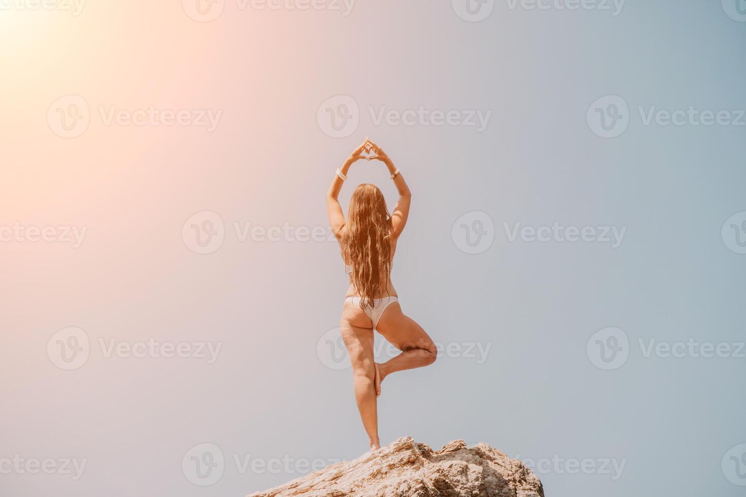 Frau Meer Yoga. zurück Aussicht von kostenlos Ruhe Glückseligkeit zufrieden Frau mit lange Haar Stehen auf oben Felsen mit Yoga Position gegen von Himmel durch das Meer. gesund Lebensstil draußen im Natur, Fitness Konzept. foto