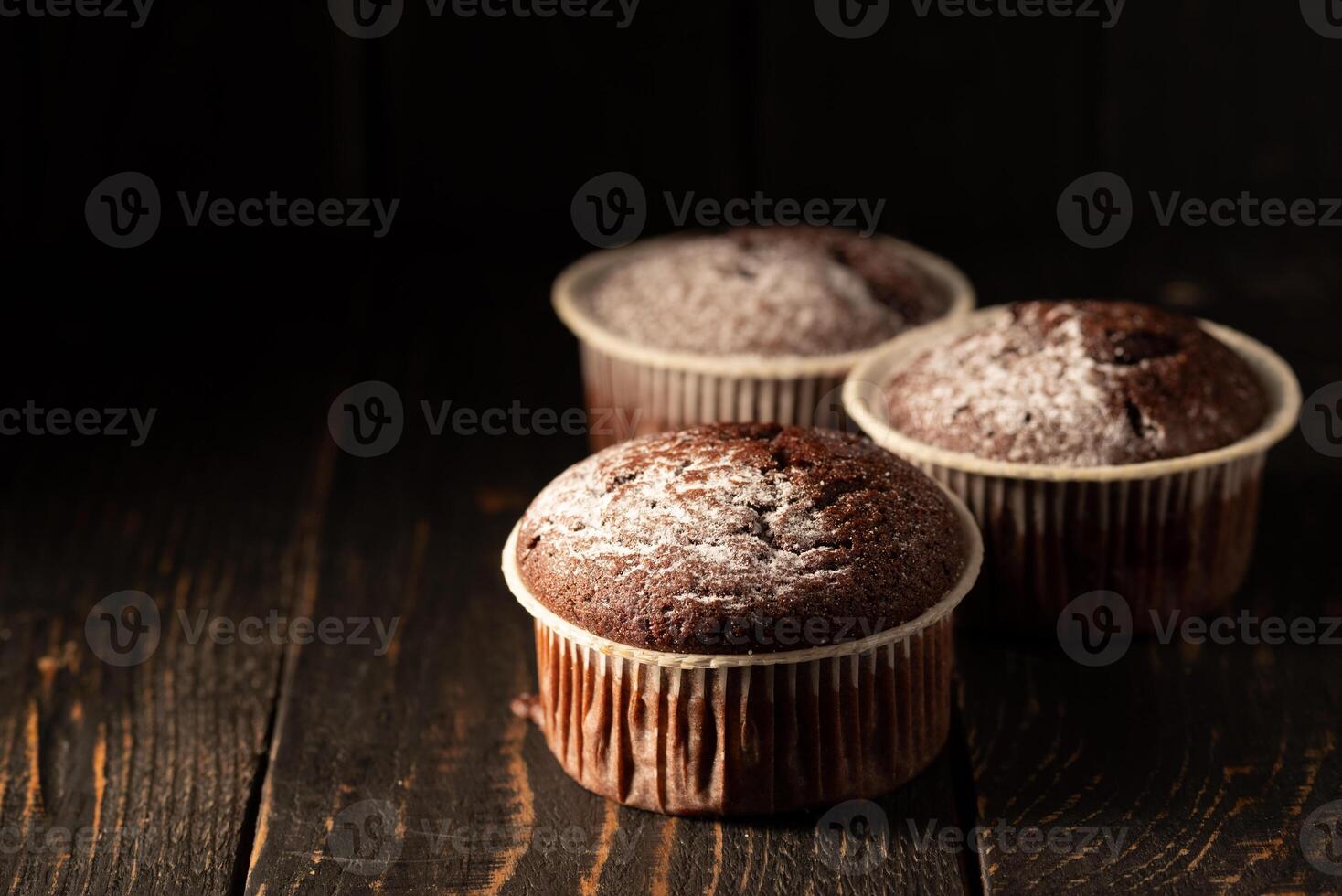 Schokolade Muffins mit pulverisiert Zucker auf ein schwarz Hintergrund. immer noch Leben schließen hoch. dunkel launisch. Essen Foto. foto