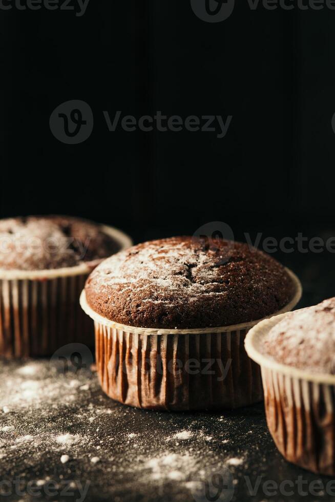 Schokolade Muffins mit pulverisiert Zucker auf ein schwarz Hintergrund. immer noch Leben schließen hoch. dunkel launisch. Essen Foto. foto